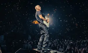Eros Ramazzotti gra na gitarze podczas koncertu, a tłum w ciemnościach trzyma zapalone telefony.