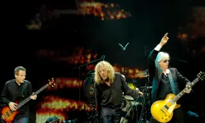 Trzech muzyków na scenie podczas koncertu Led Zeppelin. John Paul Jones gra na basie, Robert Plant śpiewa, a Jimmy Page z uniesioną ręką gra na gitarze.
