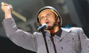 Artysta w hełmie i mundurze śpiewa do mikrofonu, podnosząc rękę z pałką. Wyraziste polskie protest songi.