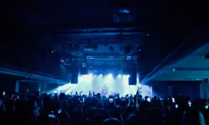 Tłum na koncercie lil tracy, ludzie nagrywają telefonami, światła sceniczne tworzą niebieską poświatę.