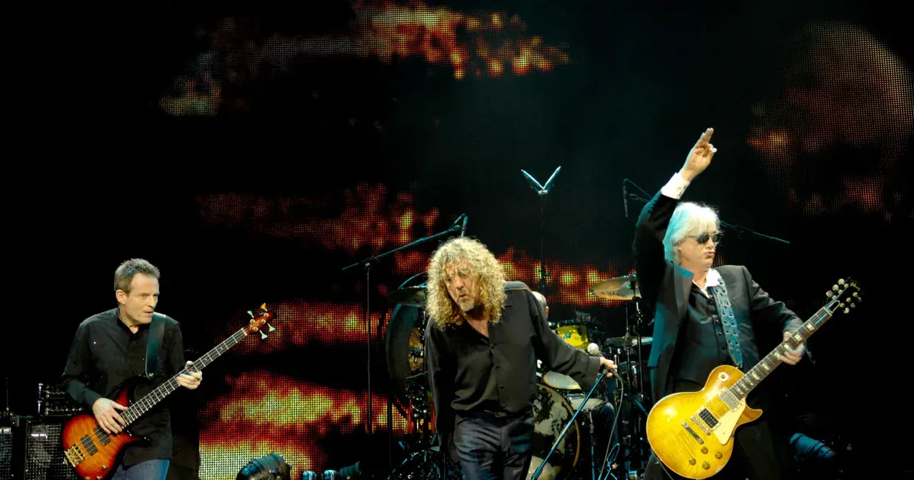 Trzech muzyków na scenie podczas koncertu Led Zeppelin. John Paul Jones gra na basie, Robert Plant śpiewa, a Jimmy Page z uniesioną ręką gra na gitarze.