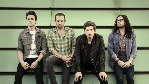 Czterech członków zespołu Kings of Leon siedzi na tle zielonej ściany.
