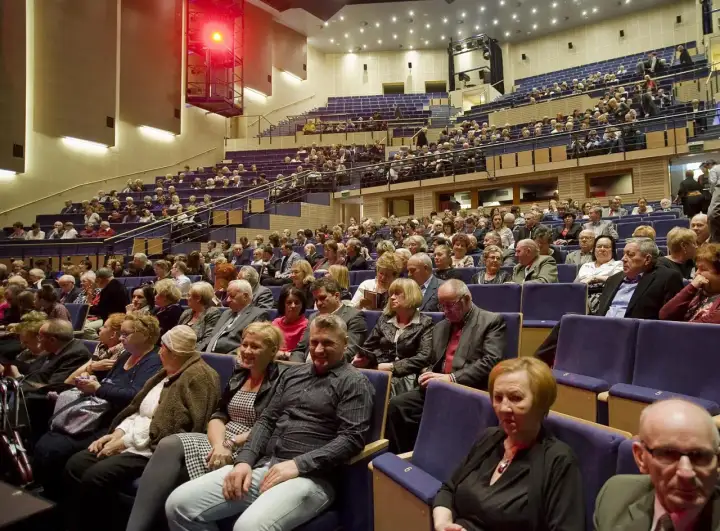Widownia filharmonii, ludzie siedzą w rzędach. Eleganckie stroje, jak się ubrać do filharmonii.